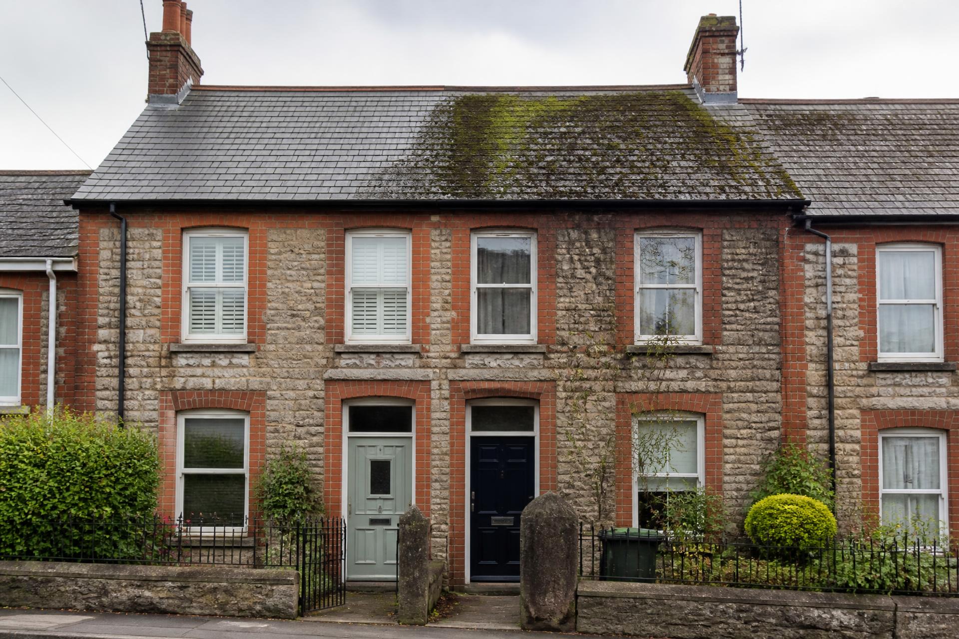 Victorian British terraced house with a slate roof half covered in moss and algae